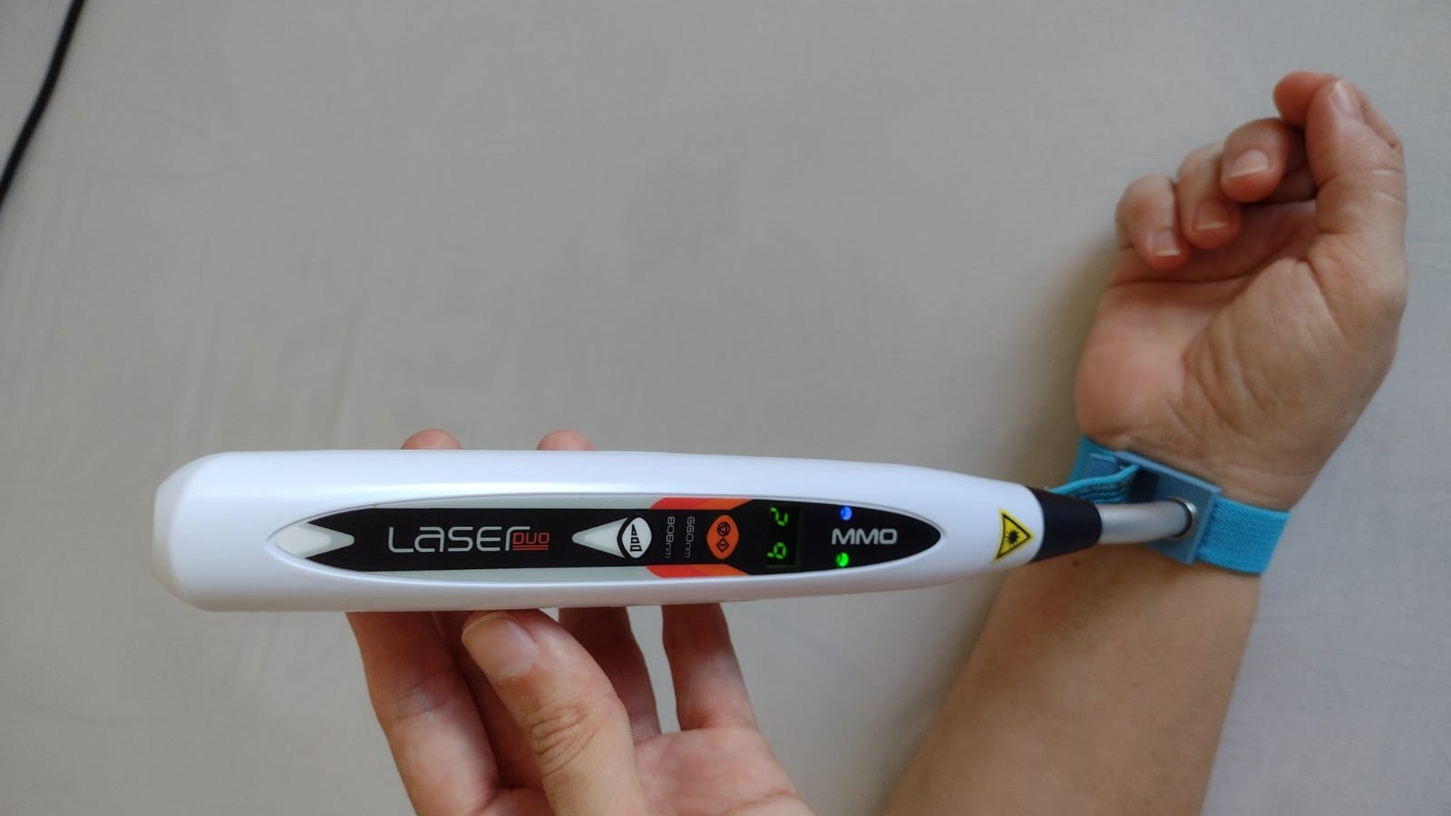 Fisioterapeuta da Fisiome realiza atendimento domiciliar em Boa Viagem, Recife, aplicando uma pulseira com laser ILIB no pulso de uma paciente confortavelmente sentada no sofá de sua residência para tratamento de fotobiomodulação sistêmica.